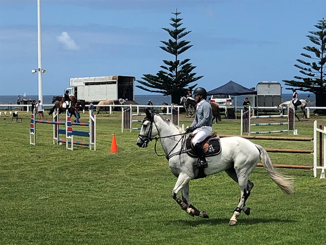 Woman riding white horse in competition on green grass at showgrounds by the sea