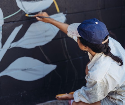 mural-artist painting white flowers and leaves onto a black brick wall